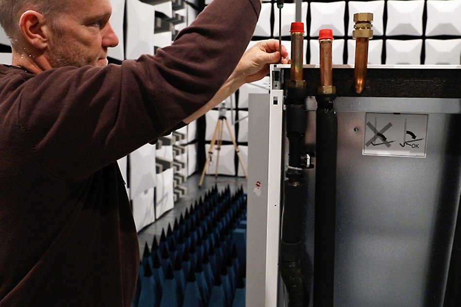 A man using a screwdriver on a heat pump inside a test chamber for electronic devices. Photo.