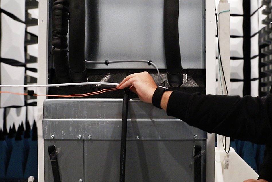 Hand reaching for cable inside a heat pump. Photo.