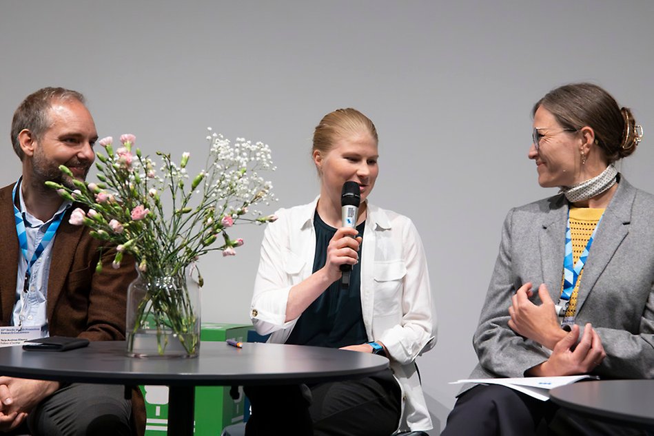 A man and two women are sitting by a table. Photo.