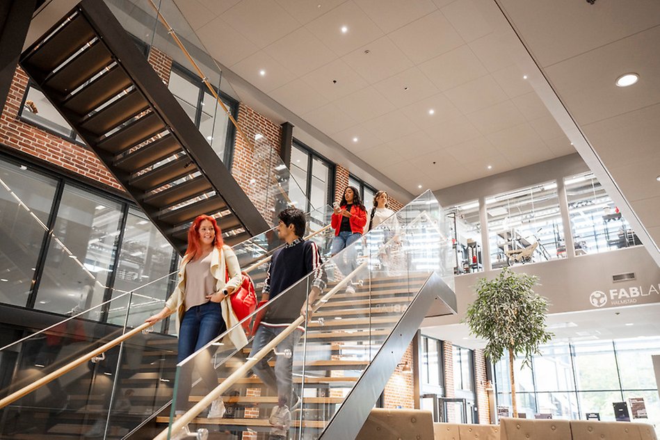 Students walking down the stairs in a building with brick walls and glass windows. Photo.