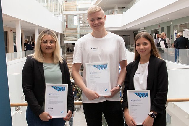 Three students are proudly posing with their diplomas in the S building.