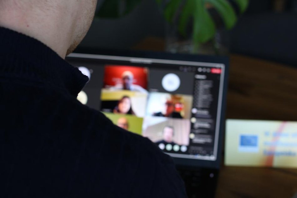En person sitter framför en dator och tittar in skärmen som visar ett antal personer som deltar i ett videomöte.