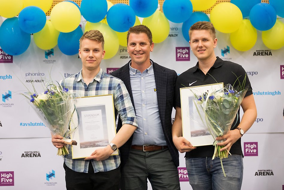Tre män, varav två stycken med diplom och blommor. Ballonger i bakgrunden.