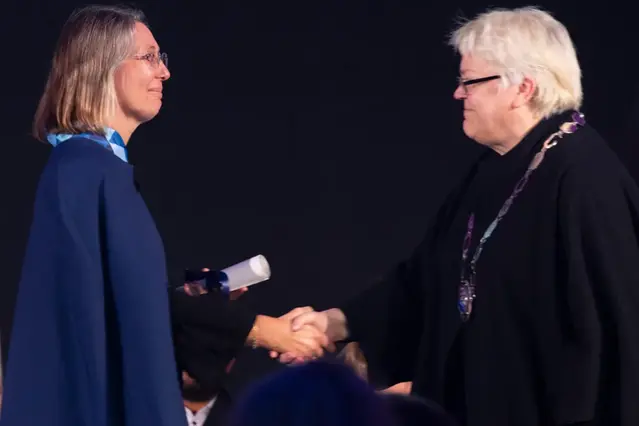 Två personer står vända mot varandra och skakar hand. Foto