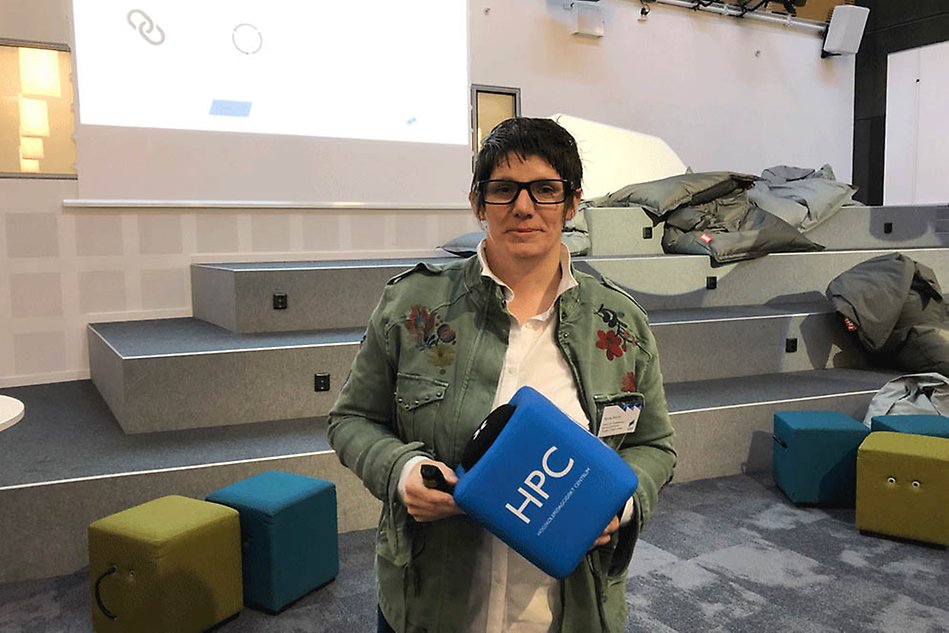 Woman with dark hair and green jacket holding a big blue cube.