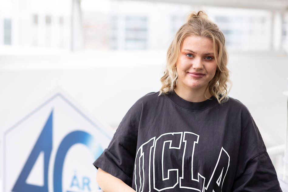 Ung blond kvinna i svart t-shirt står framför en suddig bakgrund.