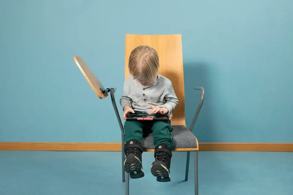 Ett barn siter på en stol med en surfplatta i knäet. Foto