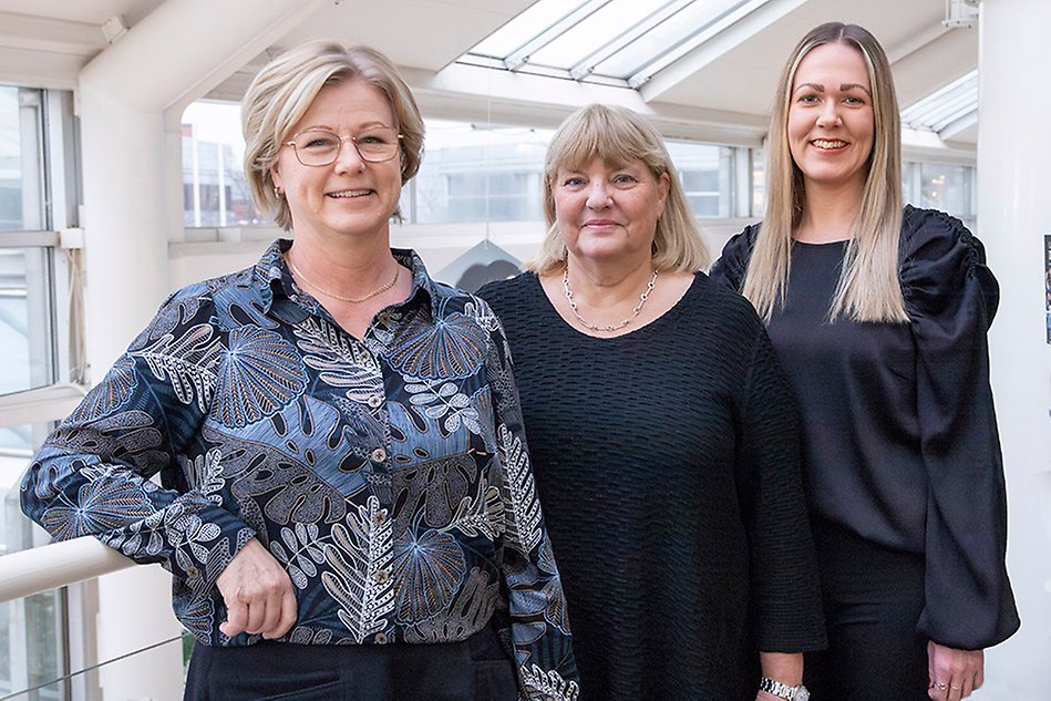 Tre kvinnor står bredvid varandra, ler och tittar in i kameran. Foto.