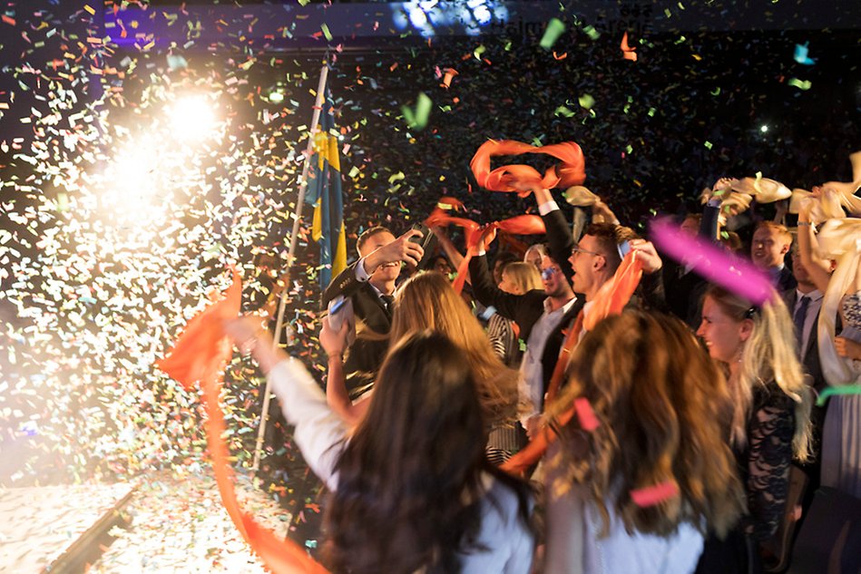 Glada studenter med fina kläder firar sin examen med konfetti