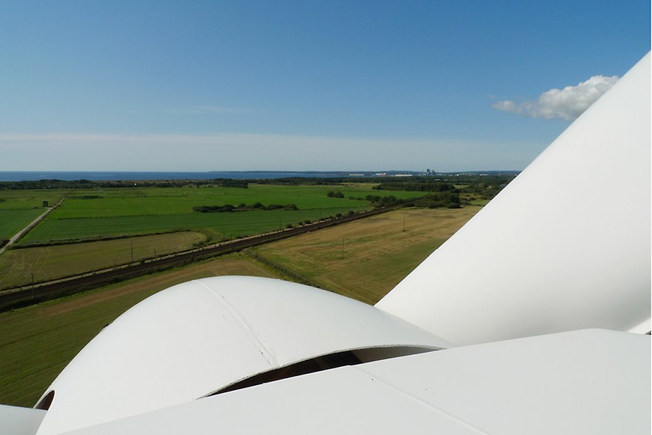 A wind turbine propeller seen from above, green and yellow fields below. Photo.