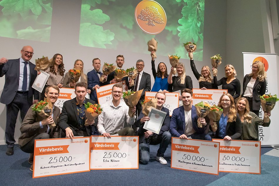 Gruppbild med många personer som tittar in i kameran och ser glada ut. Flera av dem har blomsterbuketter och stora checkar som de håller i händerna. Några sträcker upp armarna i luften i segergest.