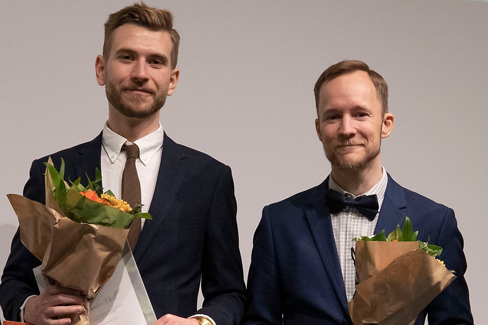 Två personer med blombuketter tittar in i kameran.