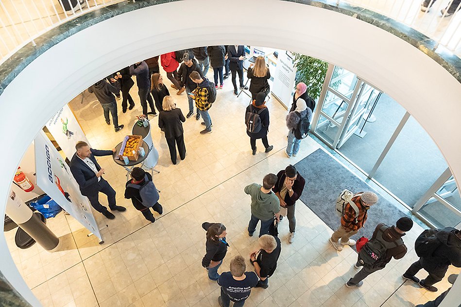 Several groups of people are standing spread out in the entrance to a building talking to each other. The photo is taken from above.