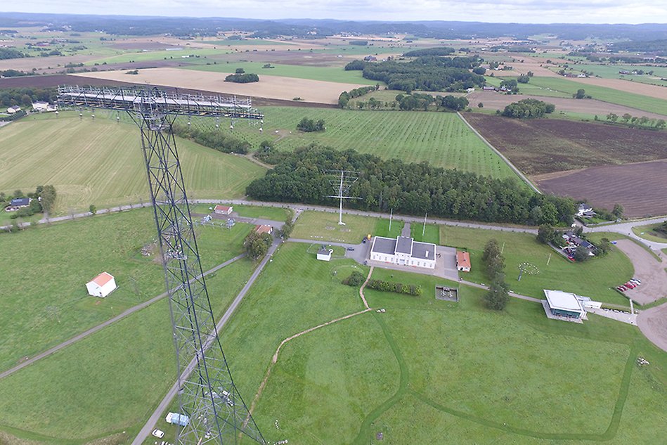 Flygbiild över grönt gräsområde, vit byggnad, radiomaster.