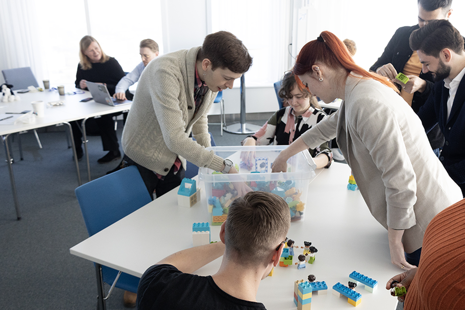 Tre personer gräver i en plastlåda med lego. Foto.