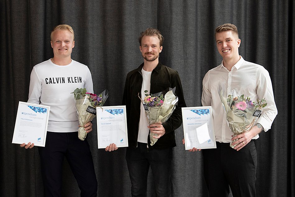 Three smiling men standing next to each other, each one of them is holding a diploma and flowers. Photo.