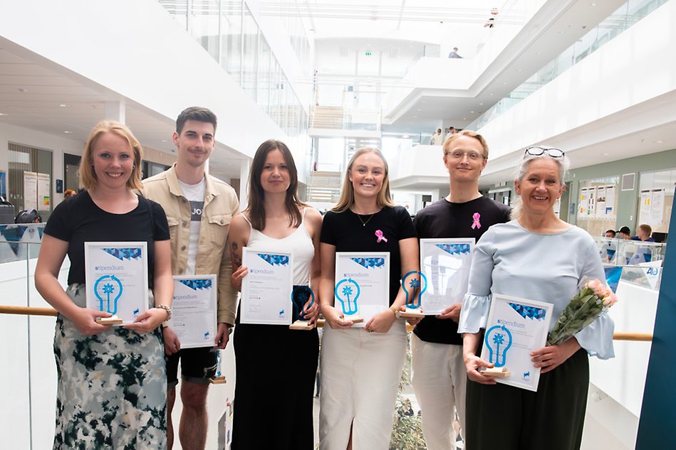 Sex glada studenter håller upp sina diplom och ler mot kameran. De står i hus S på en balkong. Foto.