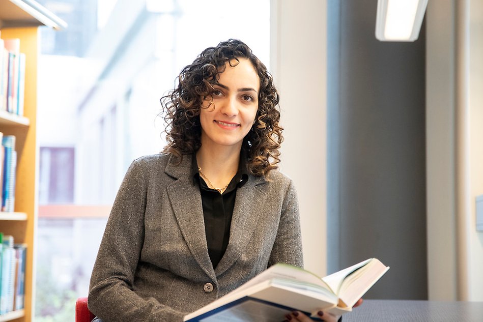 Photo of a woman holding a book while looking in to the camera. 