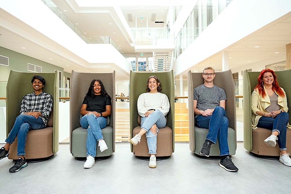 Five people, each sitting in a high armchair and look into the camera with a smile. Bright open stairwell in the background. Photo