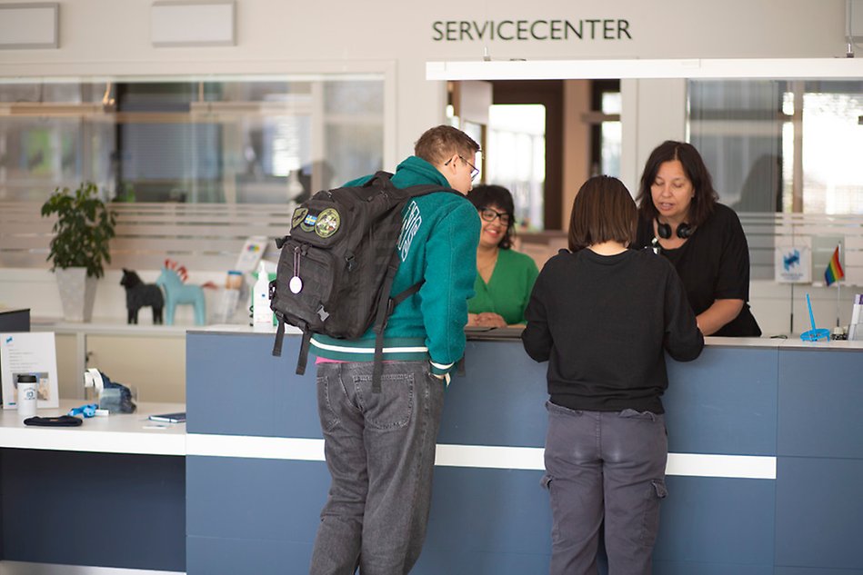 Two people are standing in Service Center talking to two women on the other side of the counter. Photo.
