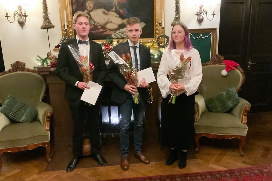 Tre finklädda personer med blommor och diplom. Fotografi.