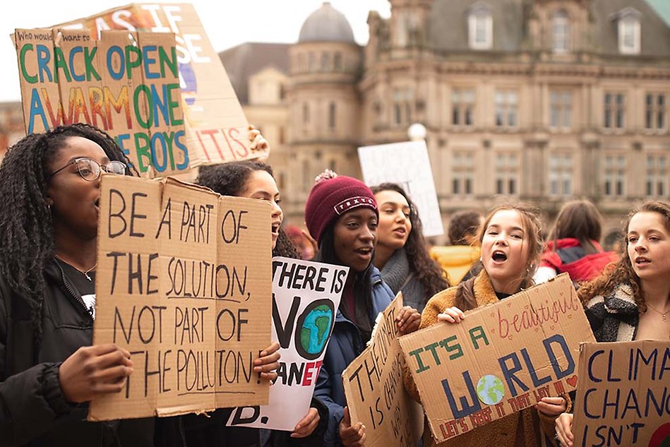 A group of youths demonstrating, holding up signs with environmental messages. Photo.