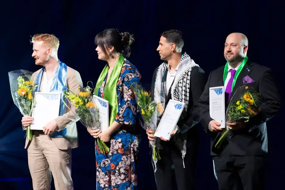 Four finely dressed young people stand on a stage with diplomas and flowers in their hands. Photo.