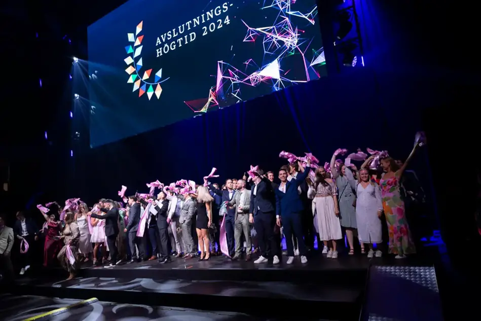 A group of well-dressed people on a stage waving colorful shawls. Photo.
