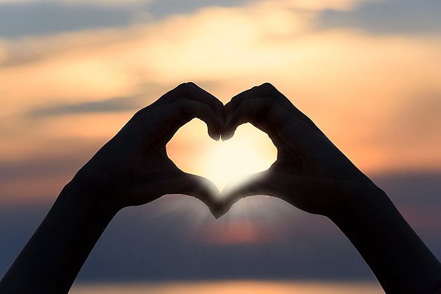 En silhuett av två händer formar ett hjärta framför en solnedgång. Foto.