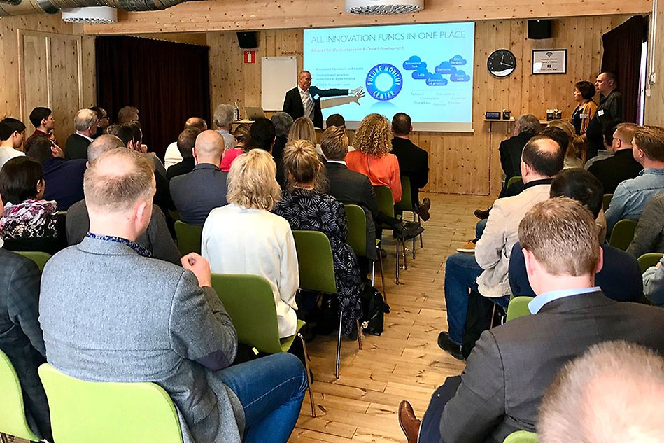A man presents a presentation slide to room full of people. Photo.