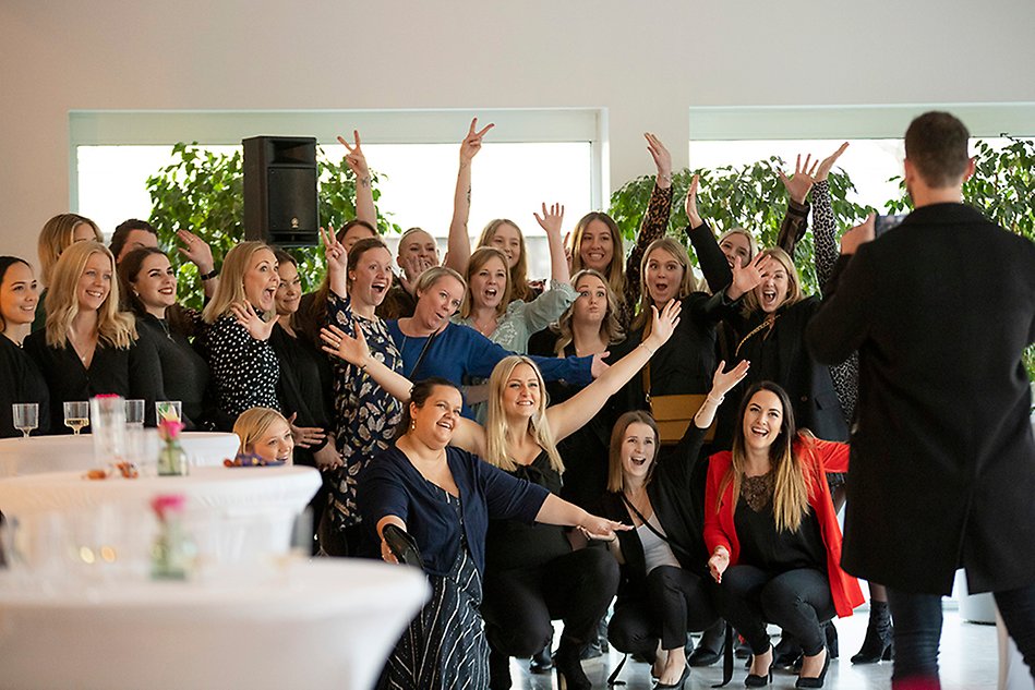 En grupp finklädda och glada studenter som skrattar, jublar och sträcker armarna i luften. Foto.