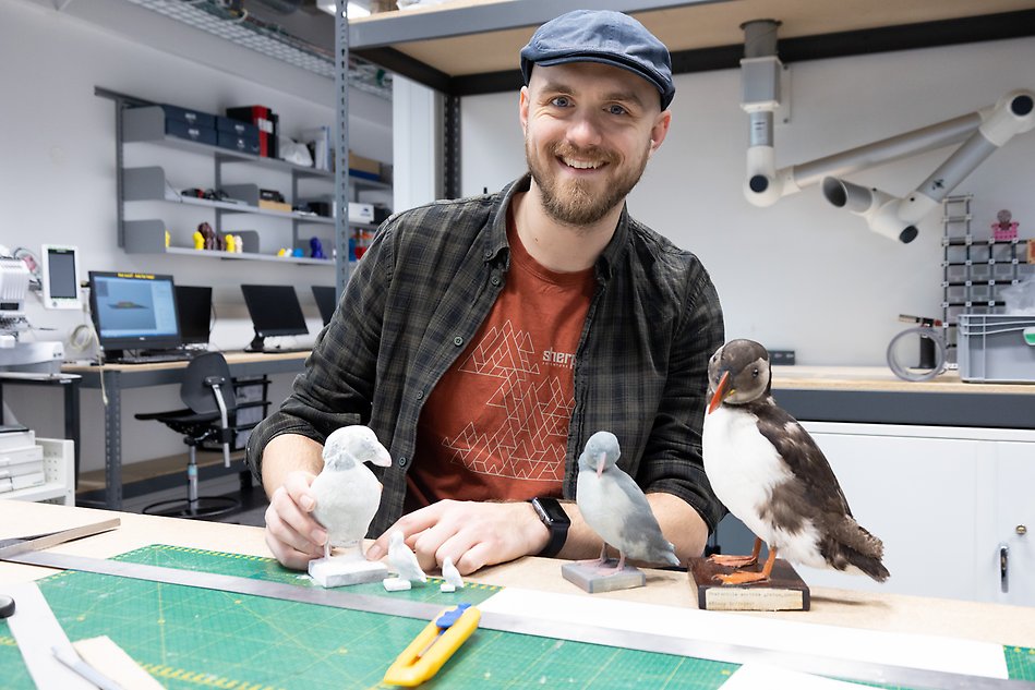 Leende kille i hatt visar upp sin 3D-printade lunnefåglar. Foto.