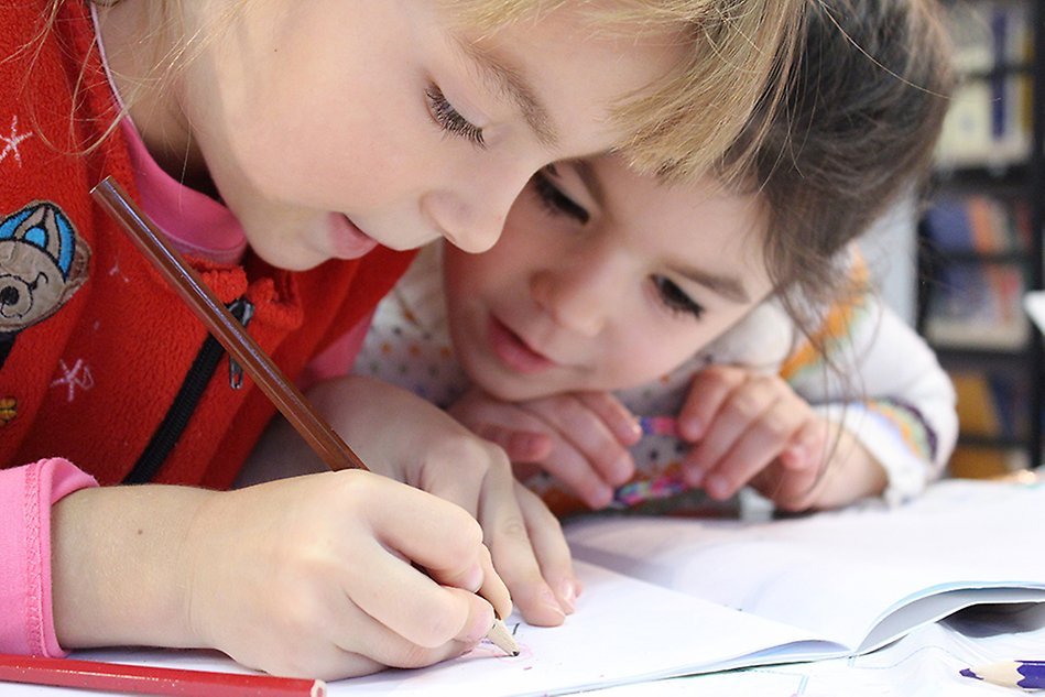Två barn som skriver i en skrivbok. Foto.