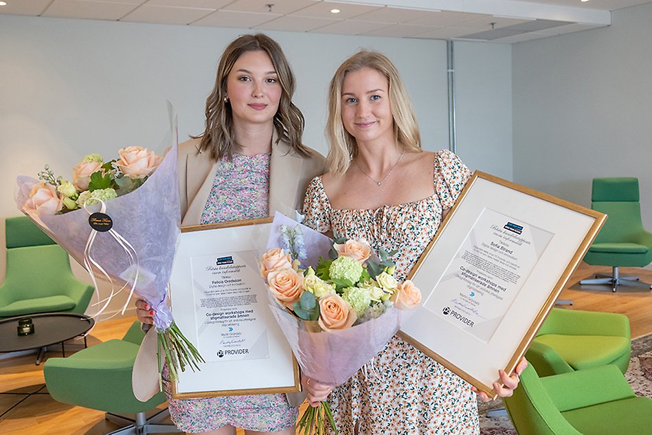 Två studenter ler och håller i blommor och diplom.