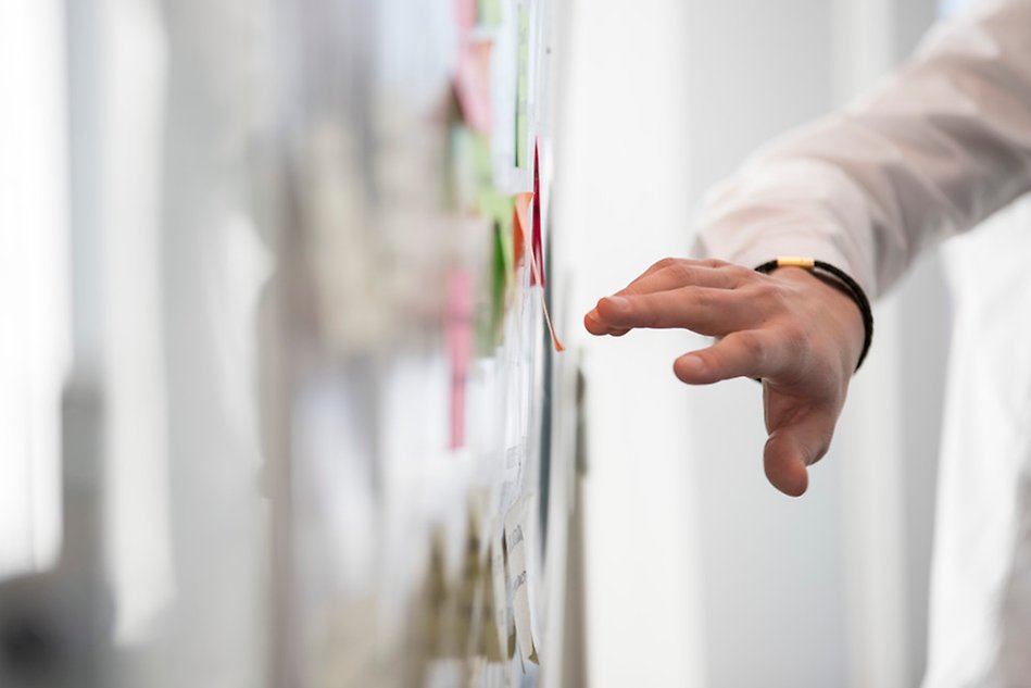 En hand som pekar på färgglada postit-lappar på en whiteboard.