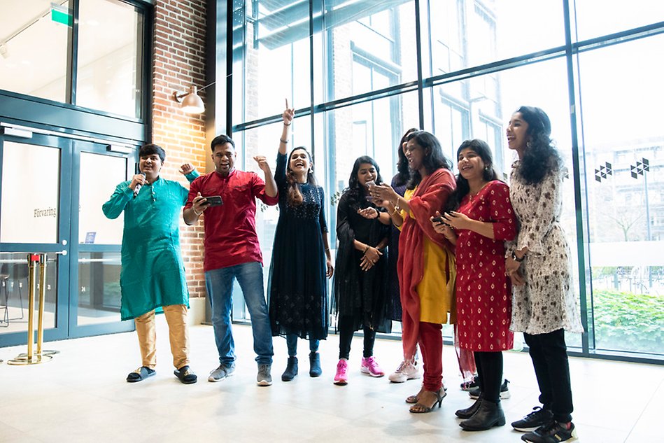 A group of people wearing colorful clothes singin together. They are holding cell phones and some people have their arms in the air. Photo.