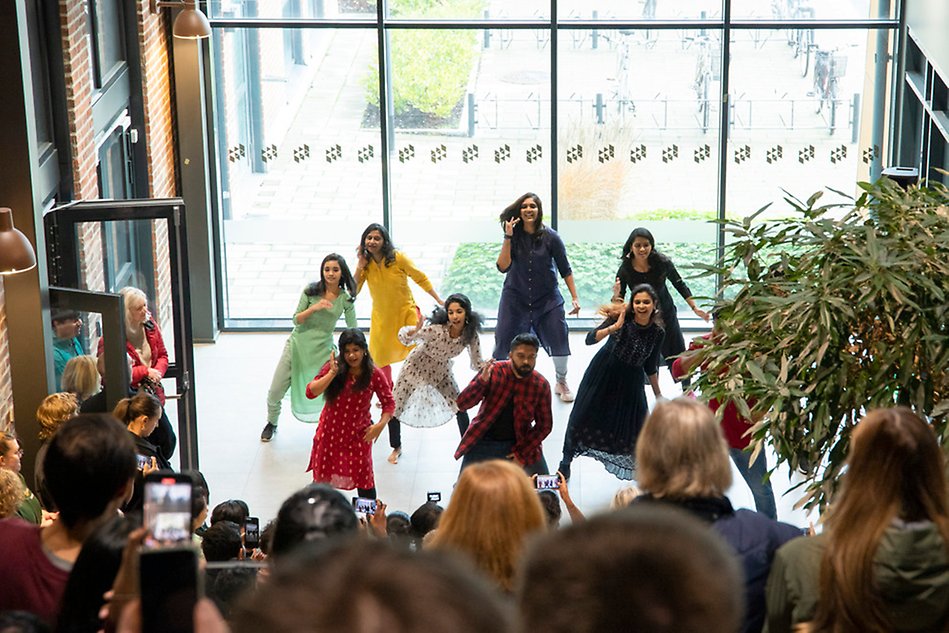 A group of people in colorful clothes. An audience is watching and many have their phones out to film. Photo.