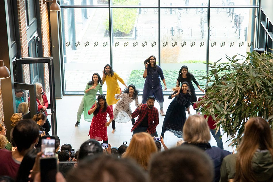 A group of people in colorful clothes. An audience is watching  and many have their phones out to film. Photo.