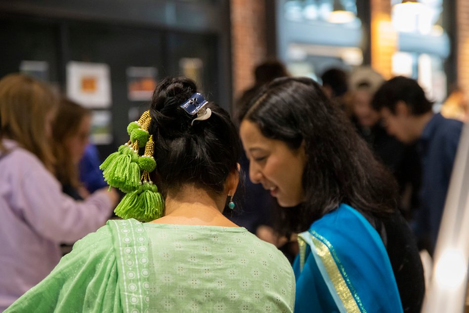 Close up of a persons hair with a green hair piece. A person is visible in the background. Photo.