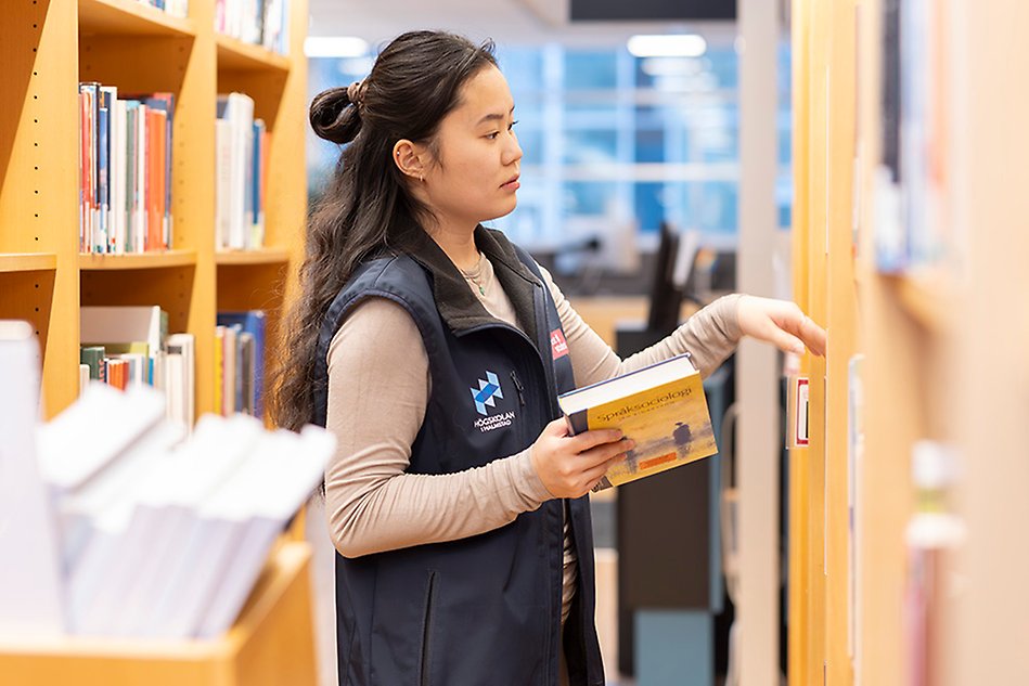En person med blå väst ställer in en bok i en bokhylla. 