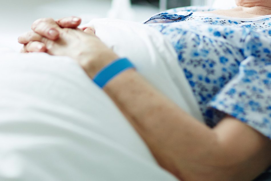 An elderly person lying in a hospital bed. Only the arm and upper body is showing. Photo.