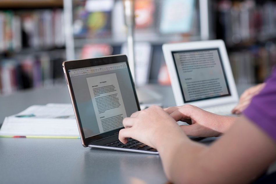 Two persons using laptops in a library. Photo.