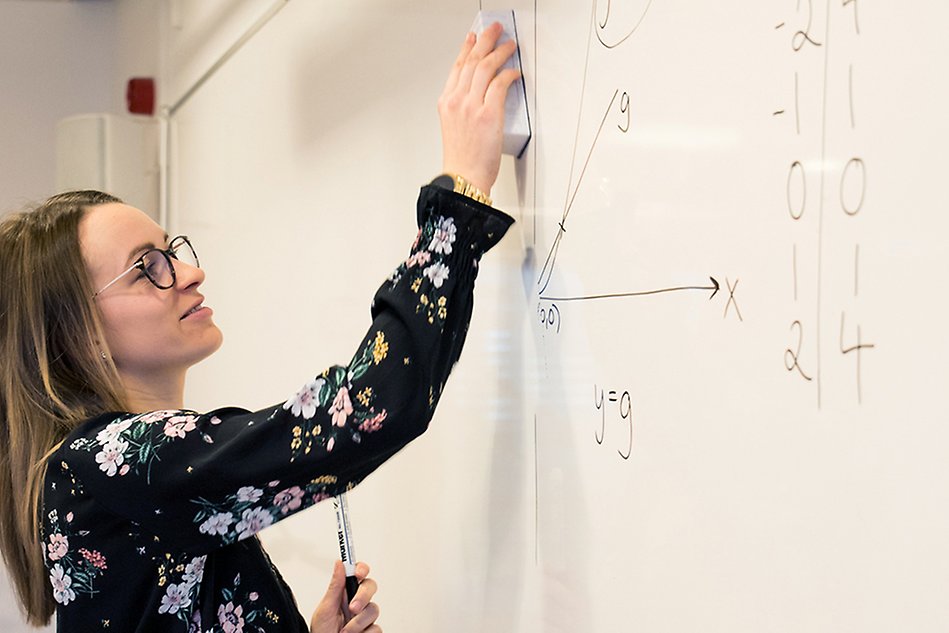 En kvinna skriver matematiska formler på en whiteboardtavla. Foto.