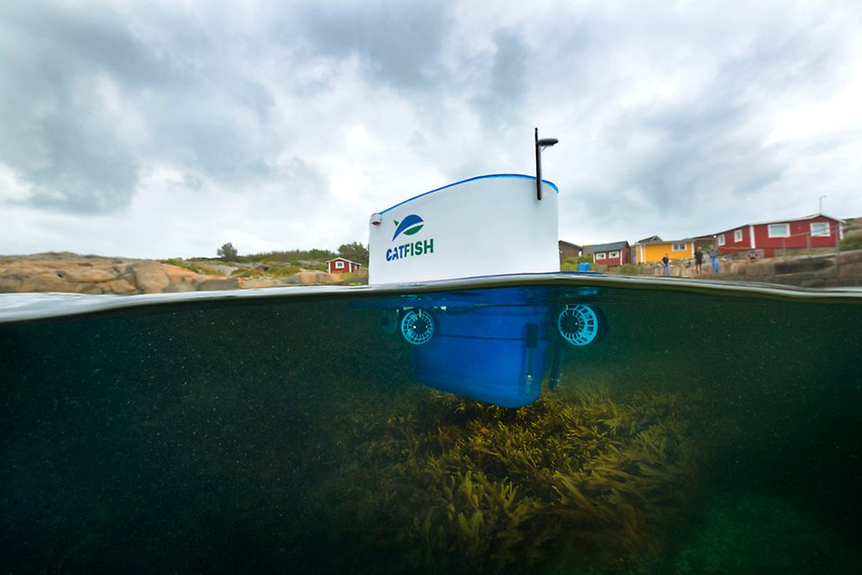 A white, oval drone floating in water. Below the surface there is seaweed.