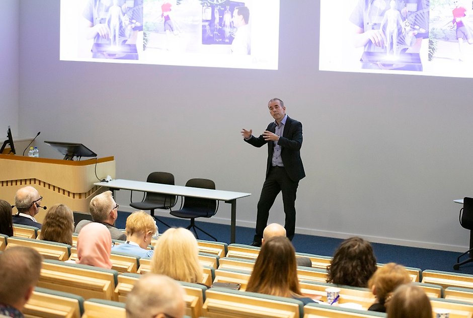 Middle-aged man speaking in front of engaged audience.