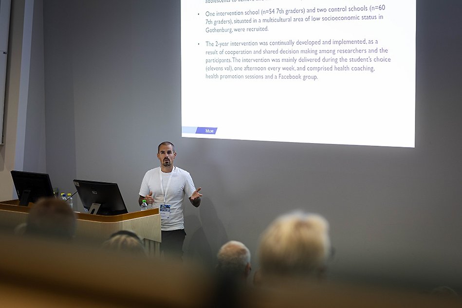 Man in t-shirt is speaking in front of a powerpoint presentation