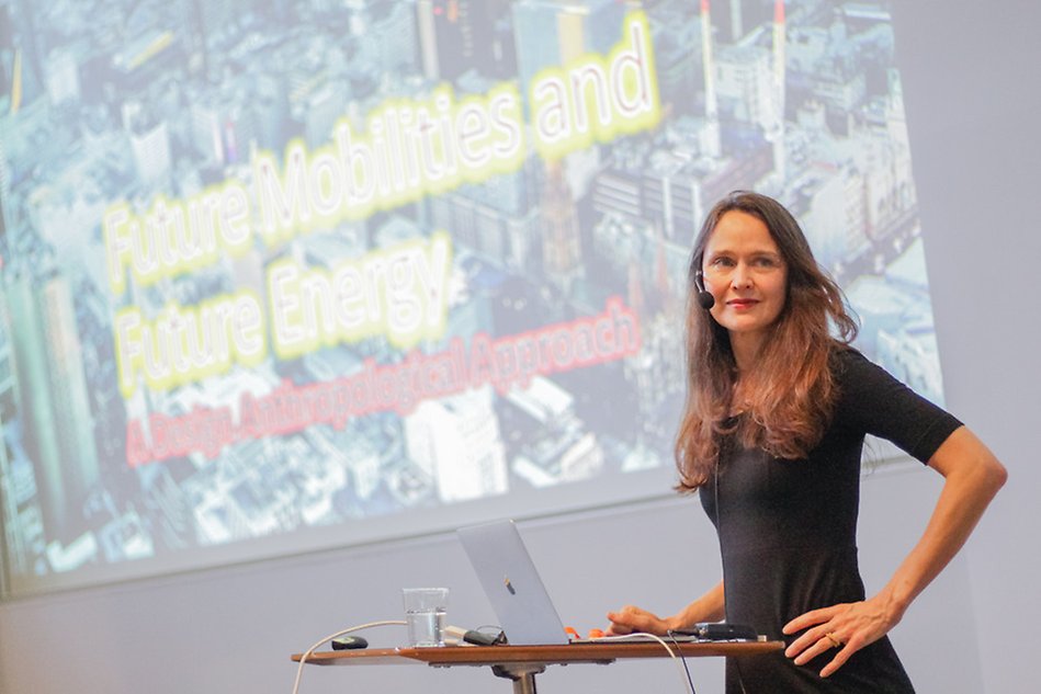 Woman dressed in black standing in front of a presentation screen. Photo.
