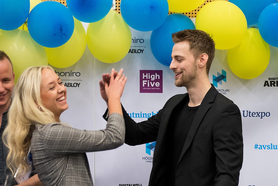 Två personer är glada och gör high five framför gula ballonger. Foto.