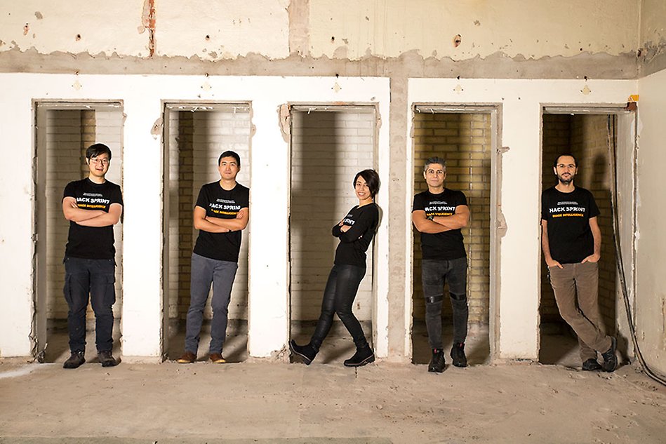 Five people standing on a row, in doorways. Smiling and looking into the camera. Photo.