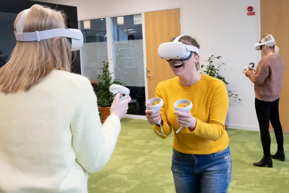 Två personer med VR-glasögon och handkontroller står mittemot varandra. Foto
